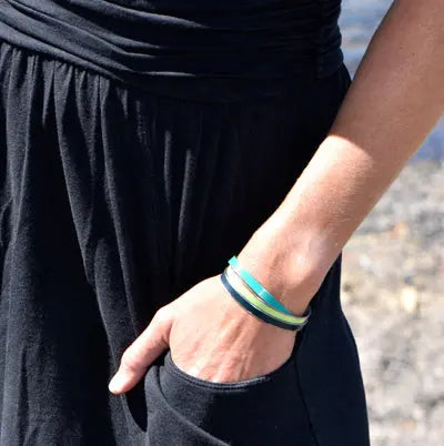 Wearing a black dress, a woman stands with her hand in her pocket,  modeling a set of three cuff bracelets all made using vintage car parts.