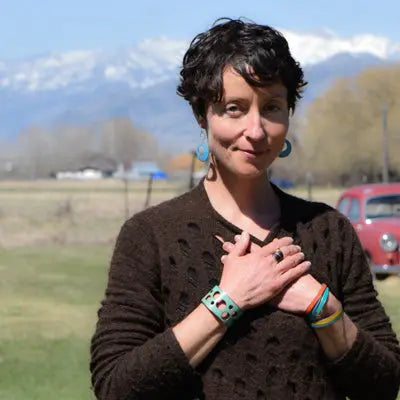 A woman with short dark hair stands outdoors, wearing a brown sweater and modeling the Ira - Ford Thunderbird bracelet. Handmade jewelry by Joyride Jewelry.
