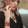 A woman with wavy blonde hair, red lipstick, and a black outfit poses . She wears geometric jewelry: an adjustable ring, red cuff bracelet with cutouts, triangular earrings, and a statement necklace all by Joyride Jewelry