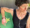 A woman with short curly hair sits. She wears a sleeveless black top,  jewelry by Joyride, an adjustable ring, and colorful bracelets, looking down to her right with a relaxed expression.